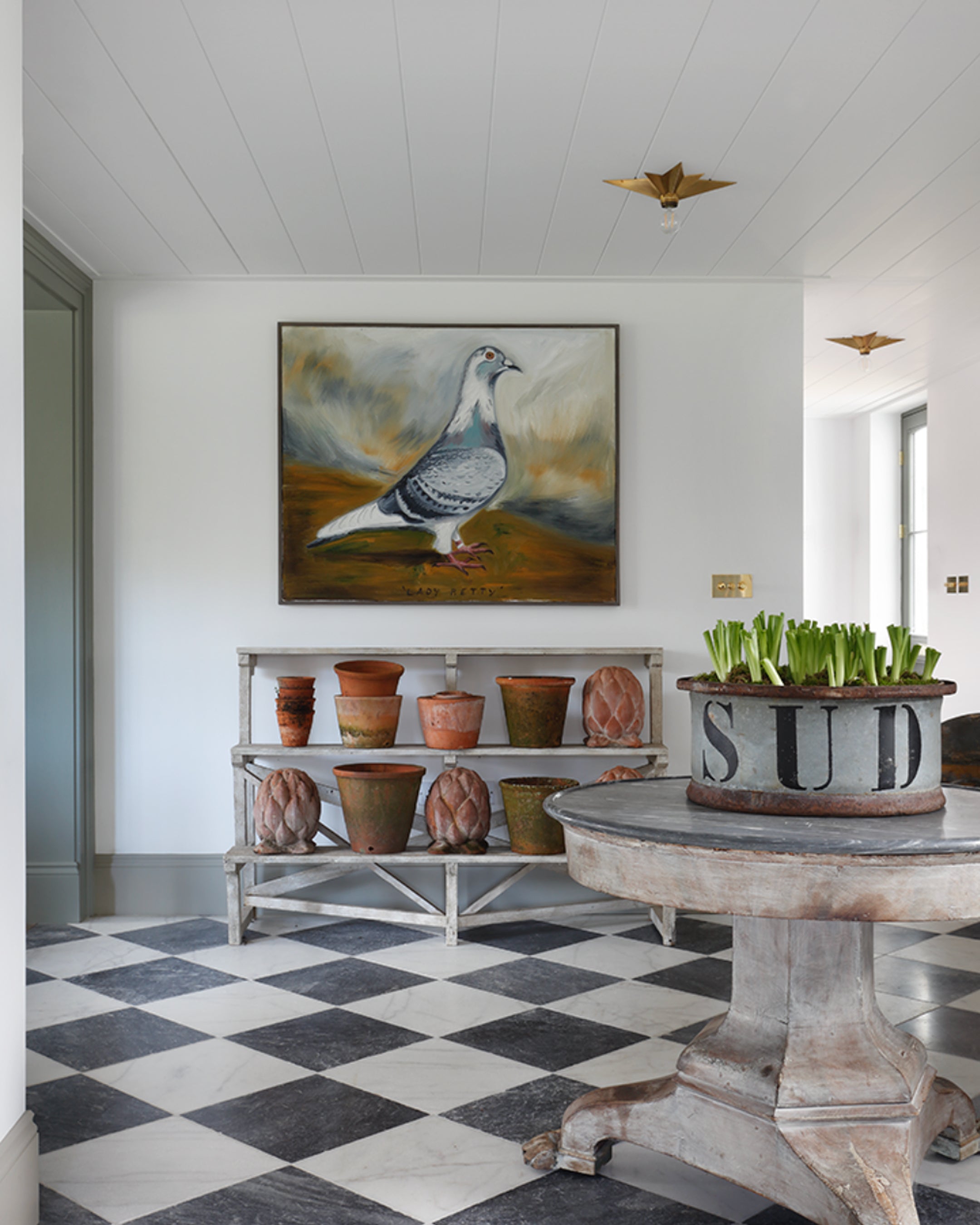 Entrance hall featuring a large artwork of a pigeon, distressed terracotta pots, and a round weathered table with a marble top