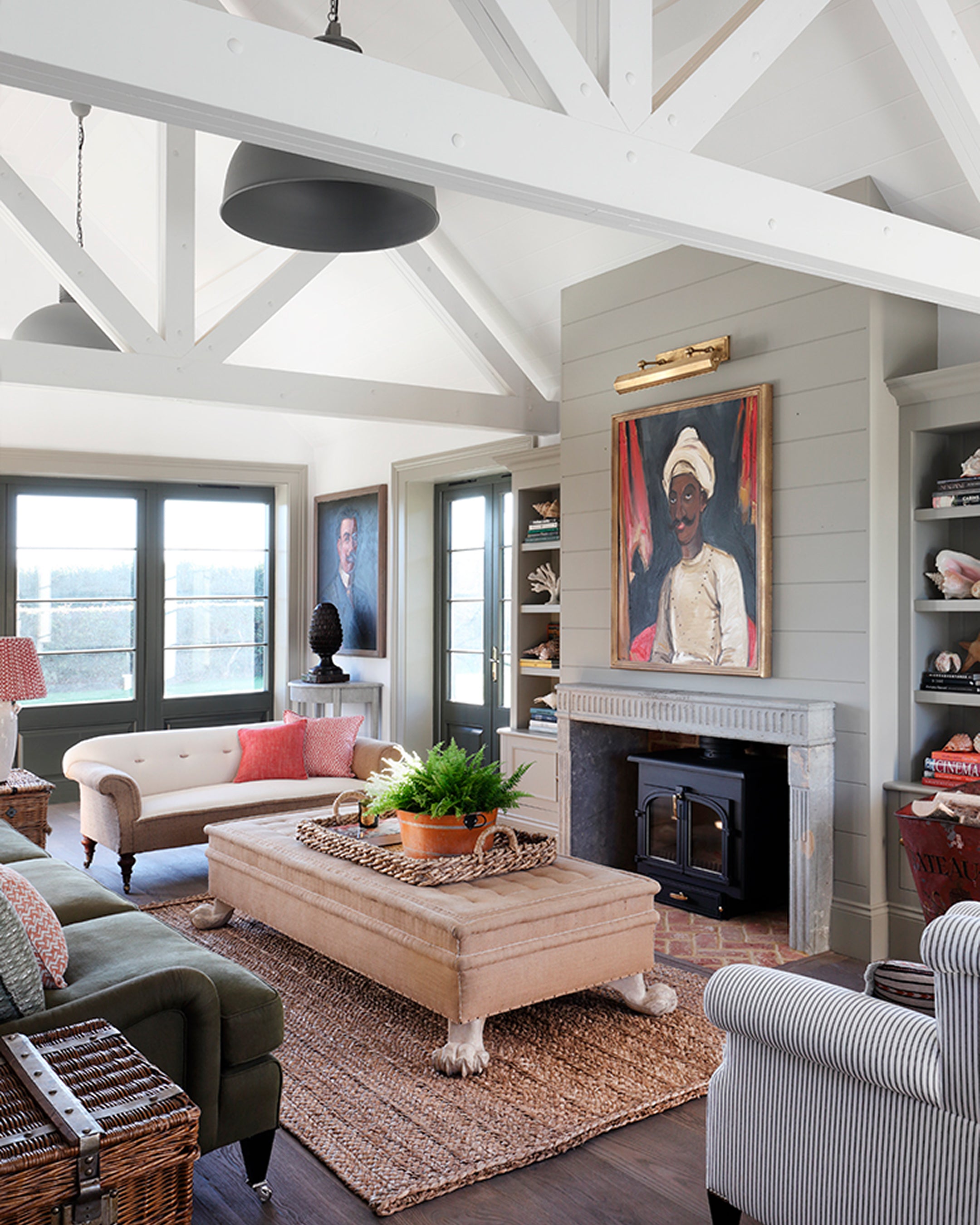 Living room featuring a vaulted ceiling with white beams, a beige tufted sofa, and a rustic stone fireplace with artwork