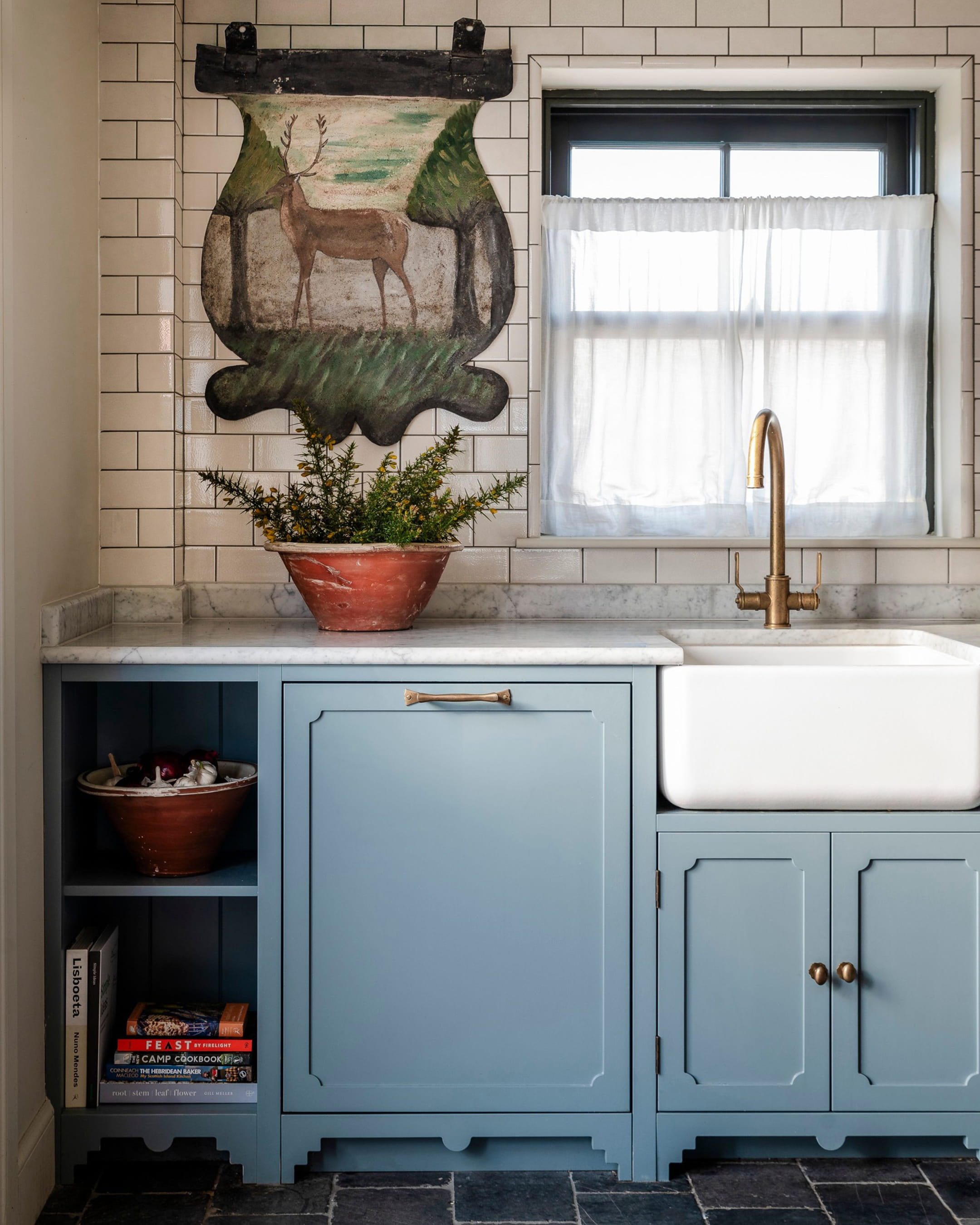 Kitchen featuring soft blue cabinetry, a white farmhouse sink, and a vintage painting of a deer above a marble countertop