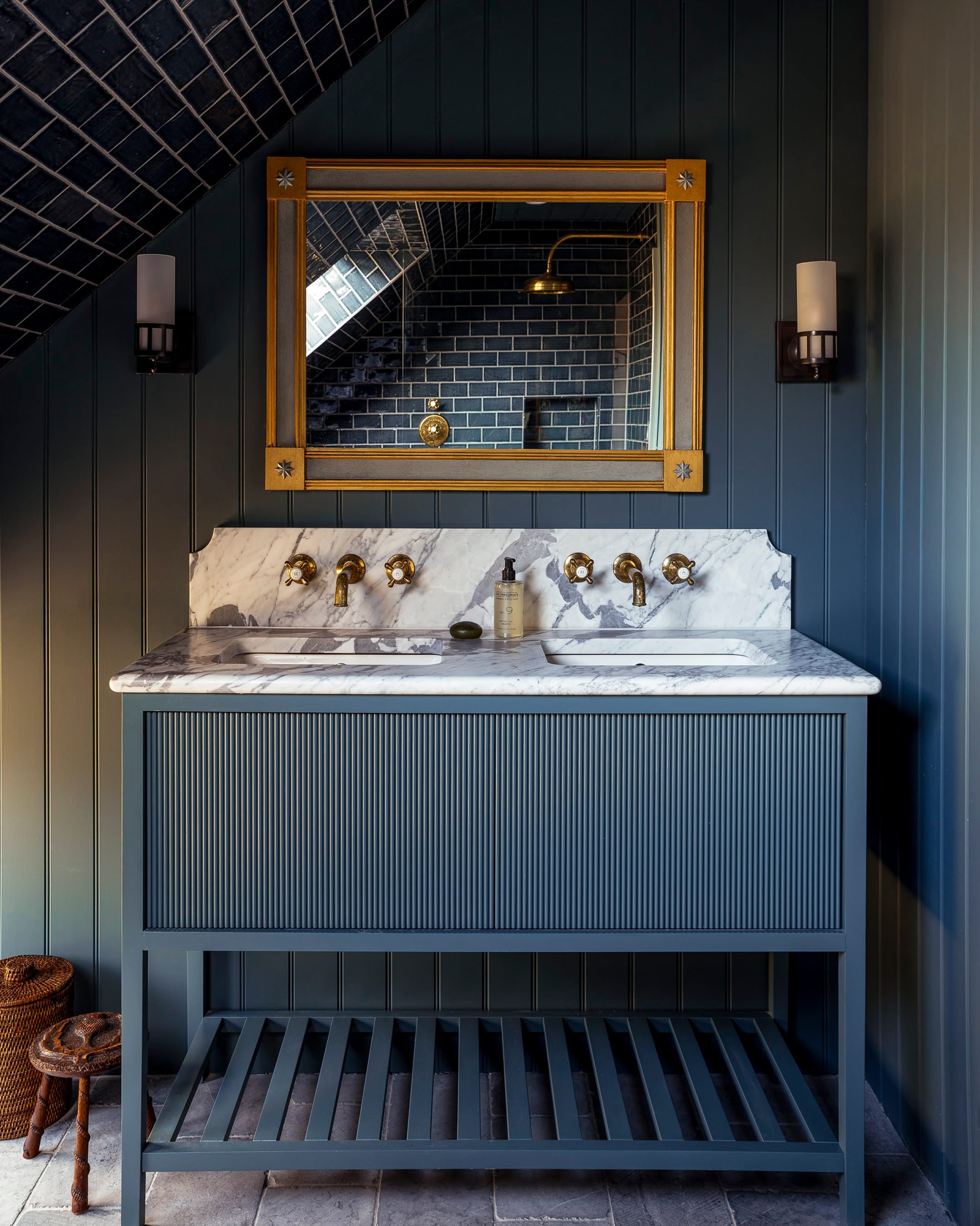 Bathroom featuring dark navy shiplap walls, a marble countertop with brass faucets, and a vintage-style gold-framed mirror