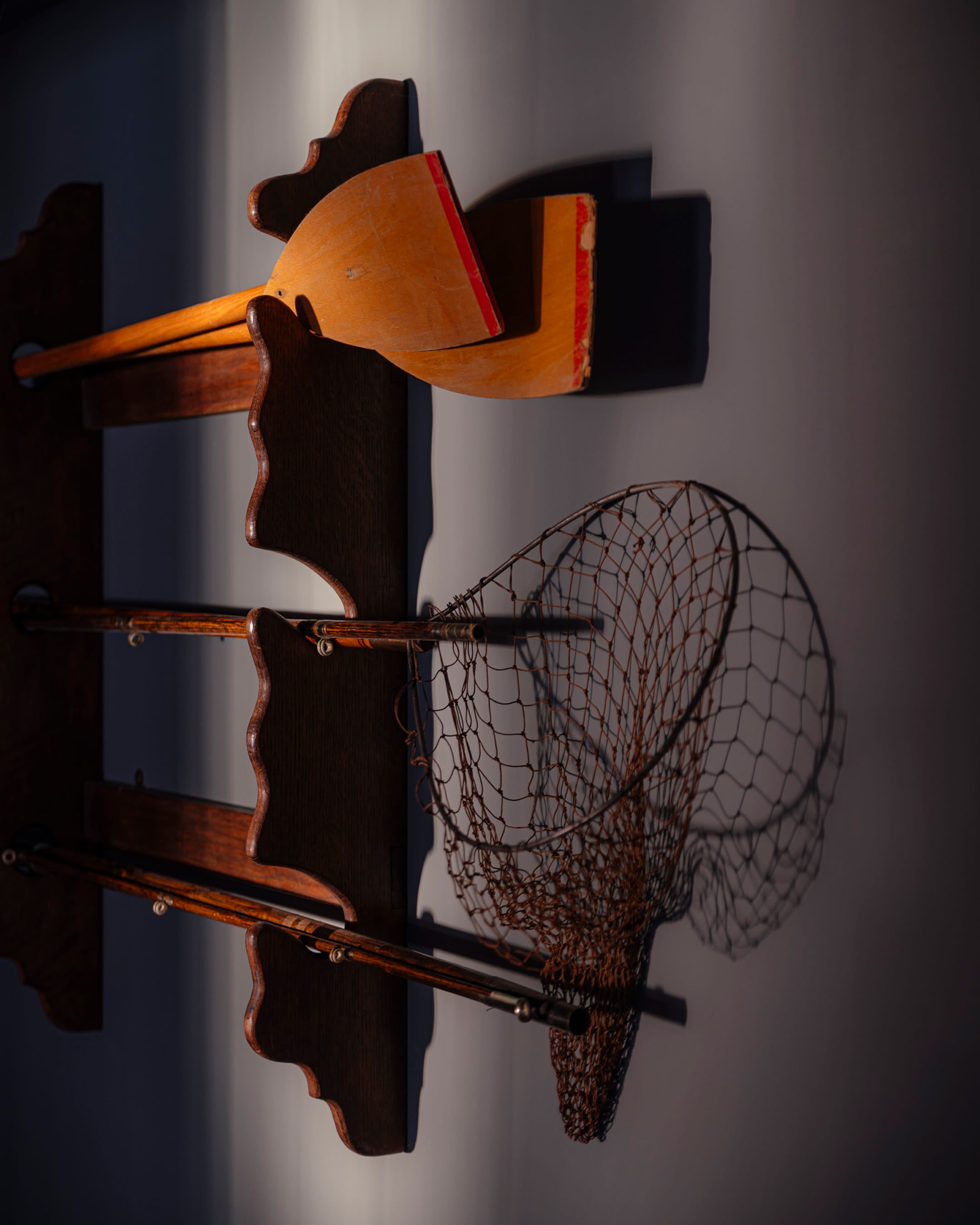 Vintage wooden paddles in vibrant orange and red, alongside a rustic fishing net against a softly lit wall